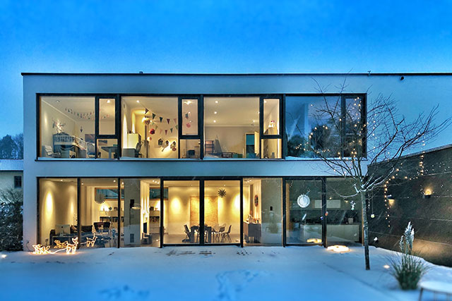 Zweistöckiges modernen Mehrfamilienhaus mit großen Fensterfronten in der Abenddämmerung.