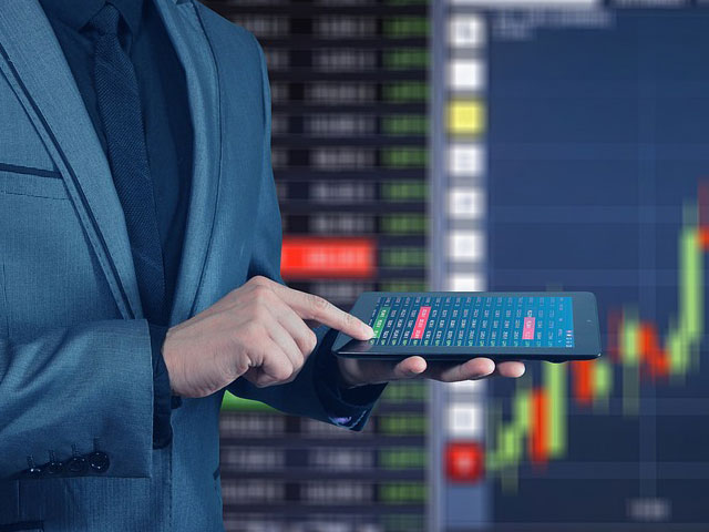 Bildausschnitt eines Manns mit Tablet und Leinwand im Hintergrund mit Börsenkursen